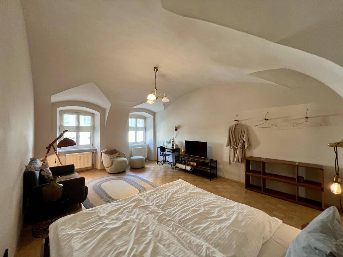 Schlafzimmer mit Parkettboden, zwei Fenstern und gemütlicher Sitzecke.