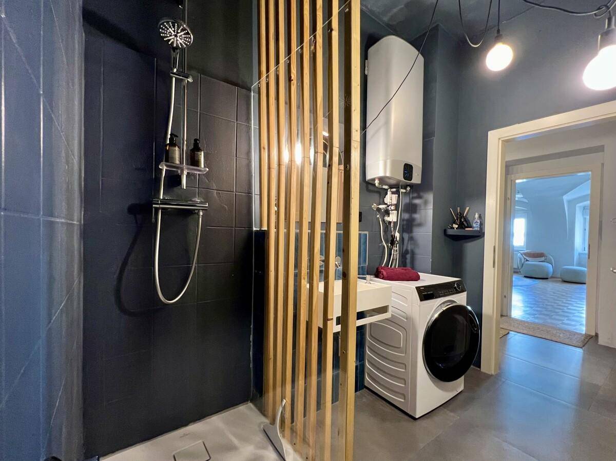 Modernes Badezimmer mit Duschbereich, Waschmaschine und blauen Fliesen.
