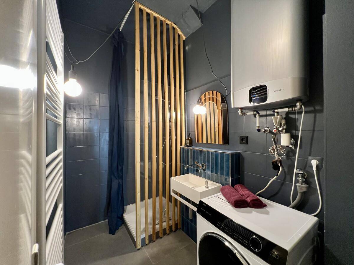 Modernes Badezimmer mit Dusche, Waschmaschine und blauen Fliesen.
