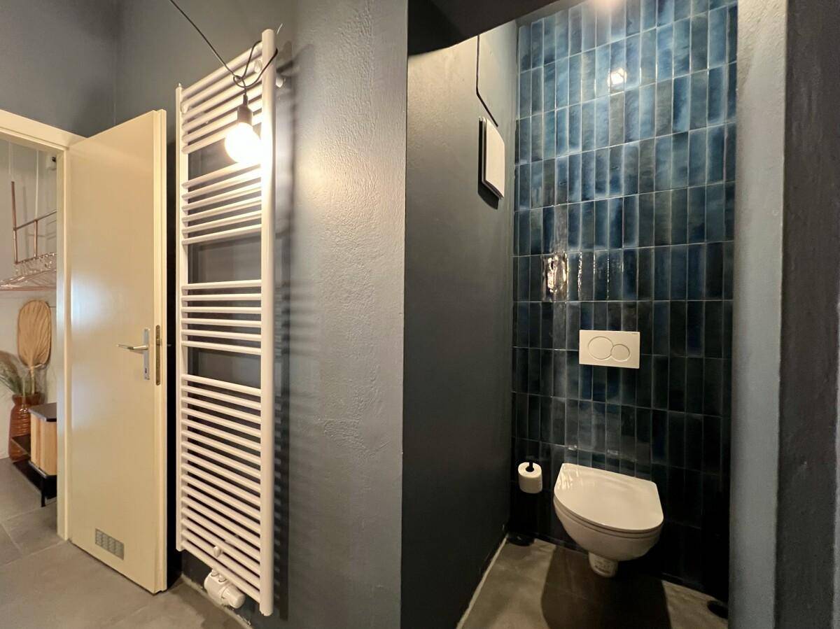 Separates WC mit Wand-WC, beheiztem Handtuchhalter und blauen Fliesen.