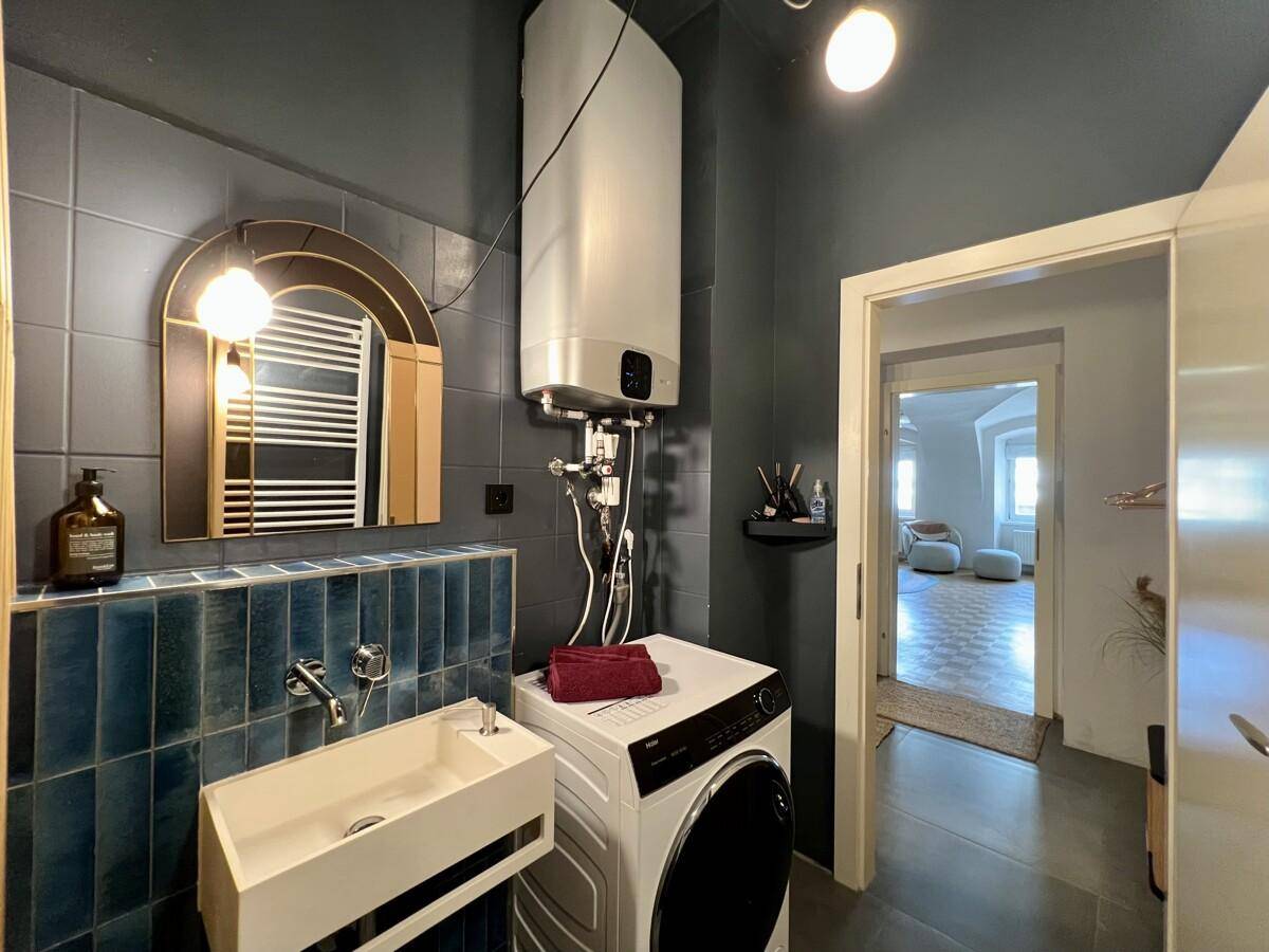 Modernes Badezimmer mit Waschmaschine, Spiegel und blauen Fliesen.