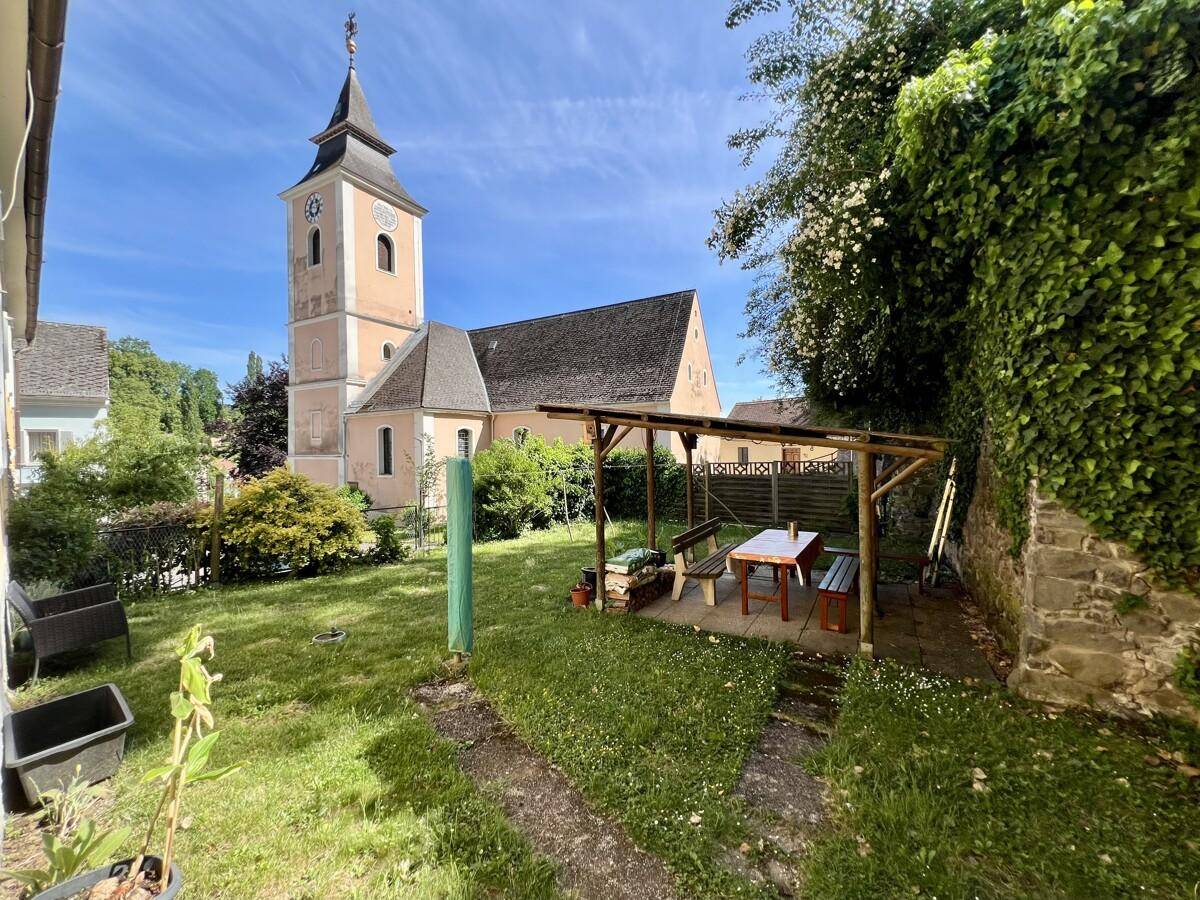 Grüner Garten mit überdachtem Sitzbereich und Blick auf die Kirche.