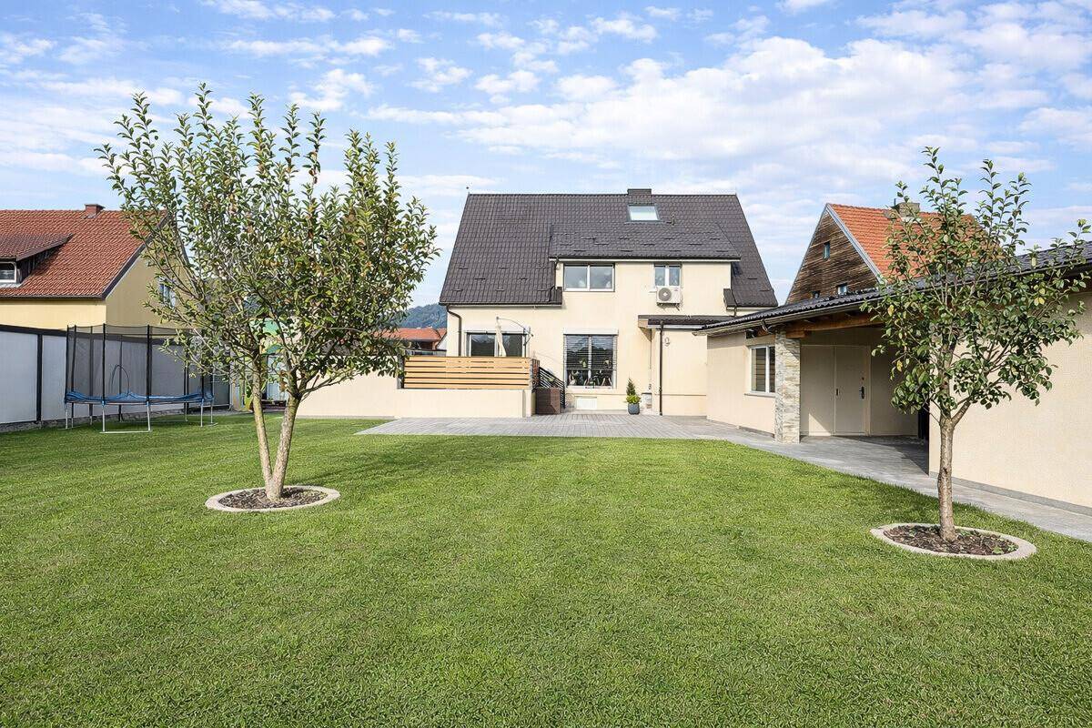 Gepflegter Garten mit Rasenfläche, jungen Obstbäumen und einer Terrasse hinter dem Haus.