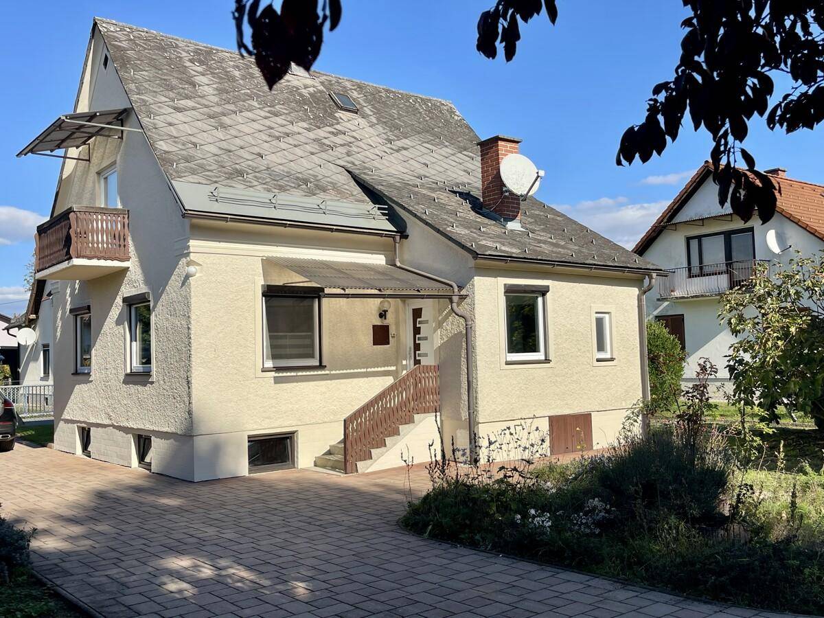 Charmantes Wohnhaus mit Balkon, gepflasterter Zufahrt und traditionellem Satteldach.