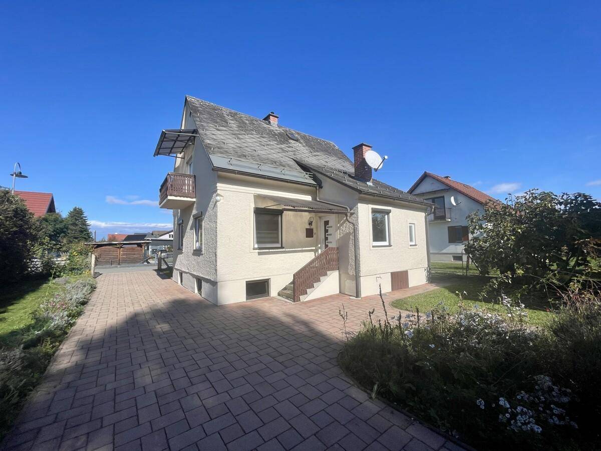 Gesamtansicht des Wohnhauses mit gepflasterter Zufahrt und Gartenbereich an einem sonnigen Tag.