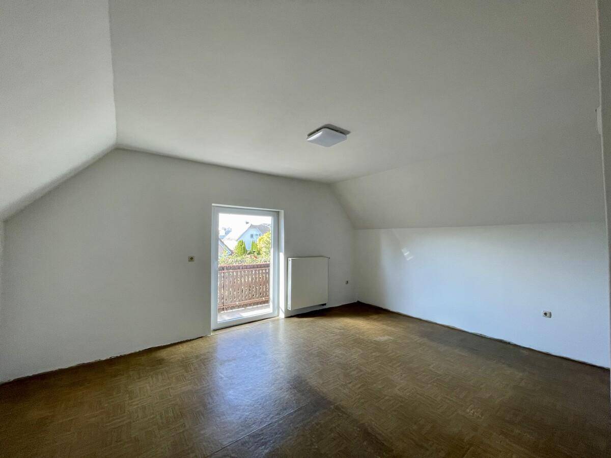Helles Dachzimmer mit Holzboden, Dachschräge und Zugang zu einem kleinen Balkon.