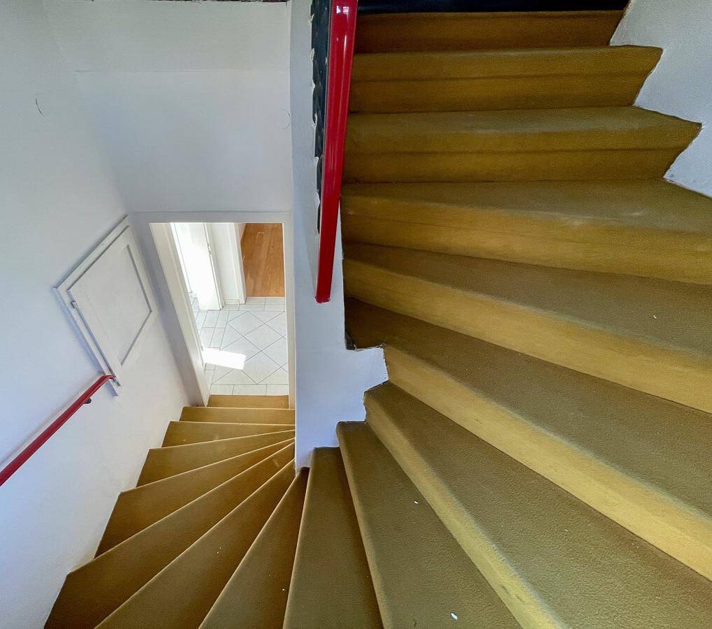 Holztreppe mit rotem Geländer, die in den unteren Bereich des Hauses führt.
