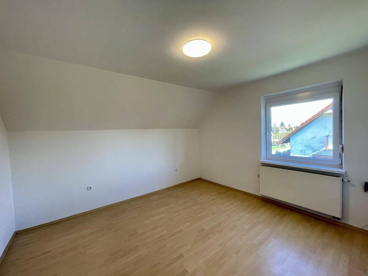 Helles Dachzimmer mit Holzboden, Dachschräge und Fenster mit Ausblick.