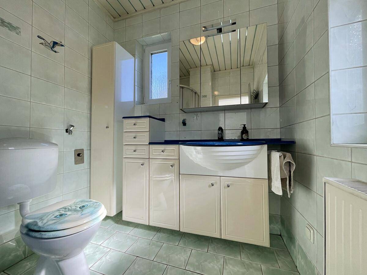 Badezimmer mit hellgrünen Fliesen, Waschtisch und WC mit Fenster.