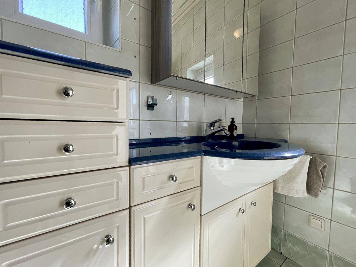 Detailansicht des Waschtischs mit blauem Akzent und Spiegelschrank im Badezimmer.