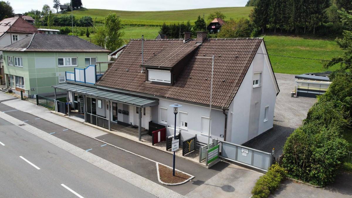 Luftaufnahme eines Wohnhauses mit Satteldach, überdachtem Eingangsbereich und grüner Umgebung.