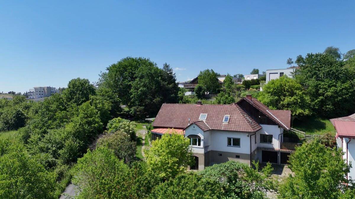 Luftaufnahme eines Hauses mit rotem Dach, umgeben von üppigem Grün und weiteren Gebäuden.