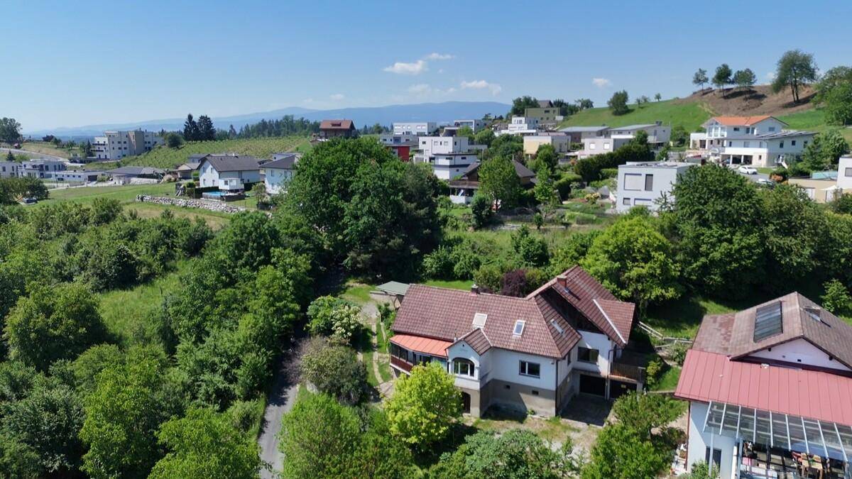 Weitläufige Luftaufnahme eines Wohngebiets mit Häusern und viel Grün in hügeliger Landschaft.