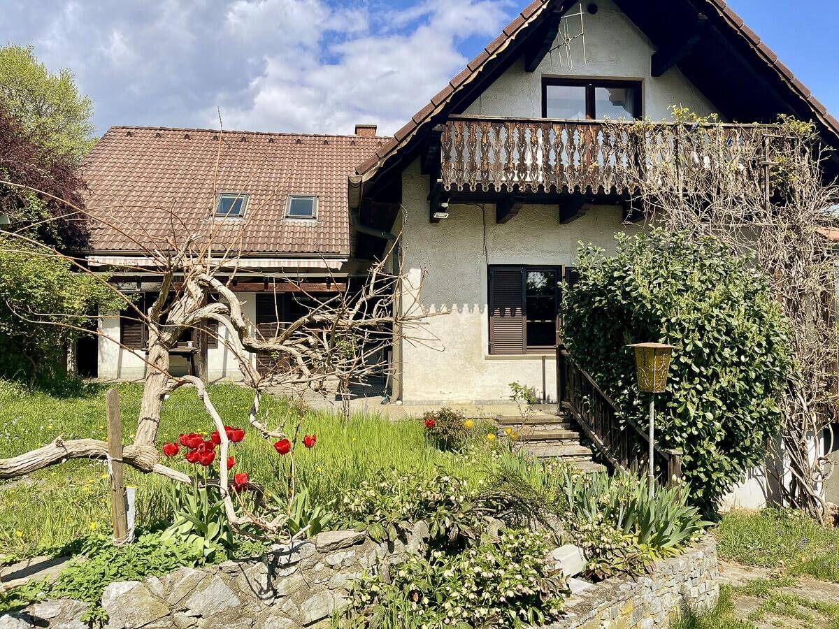 Charmantes Haus mit Balkon und blühendem Vorgarten, umgeben von üppiger Vegetation.