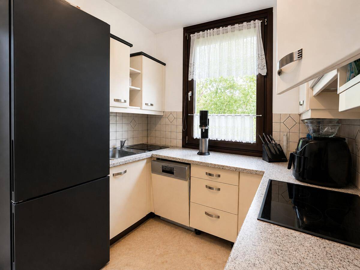 Funktionale Küche mit schwarzem Kühlschrank, beigen Schränken und Fenster.