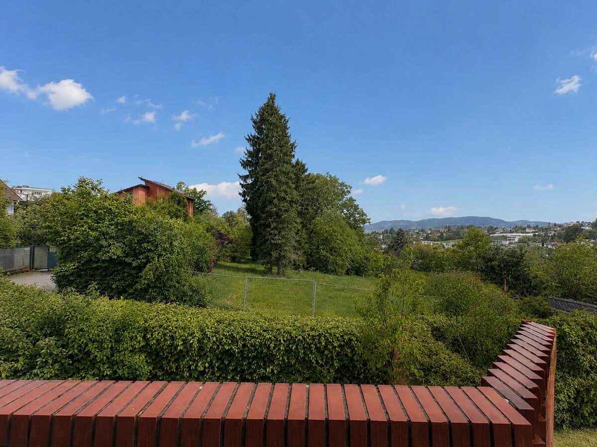 Weitläufiger Blick ins Grüne mit Bäumen und Hügeln unter blauem Himmel.