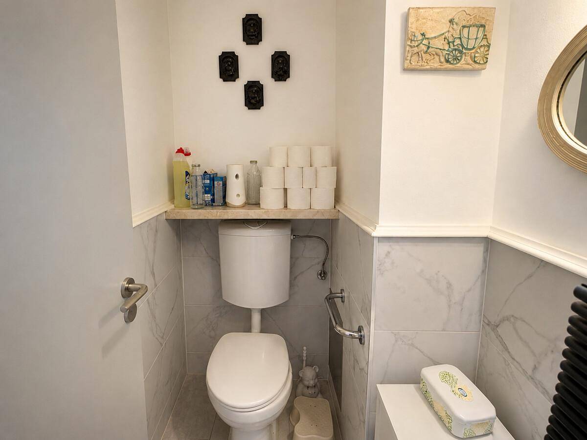 Separates WC mit Wand-WC, Handlauf und Marmorfliesen an den Wänden.