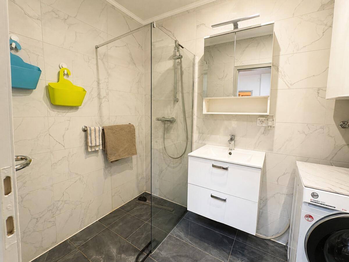 Helles Badezimmer mit Glasdusche, modernem Waschtisch und Fliesenboden.