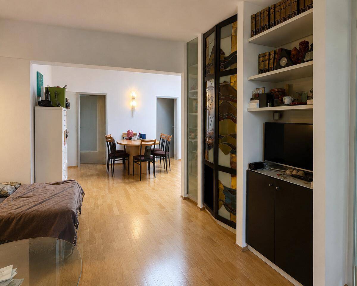 Offener Wohnbereich mit Holzboden, Bücherregal und Essbereich im Hintergrund.