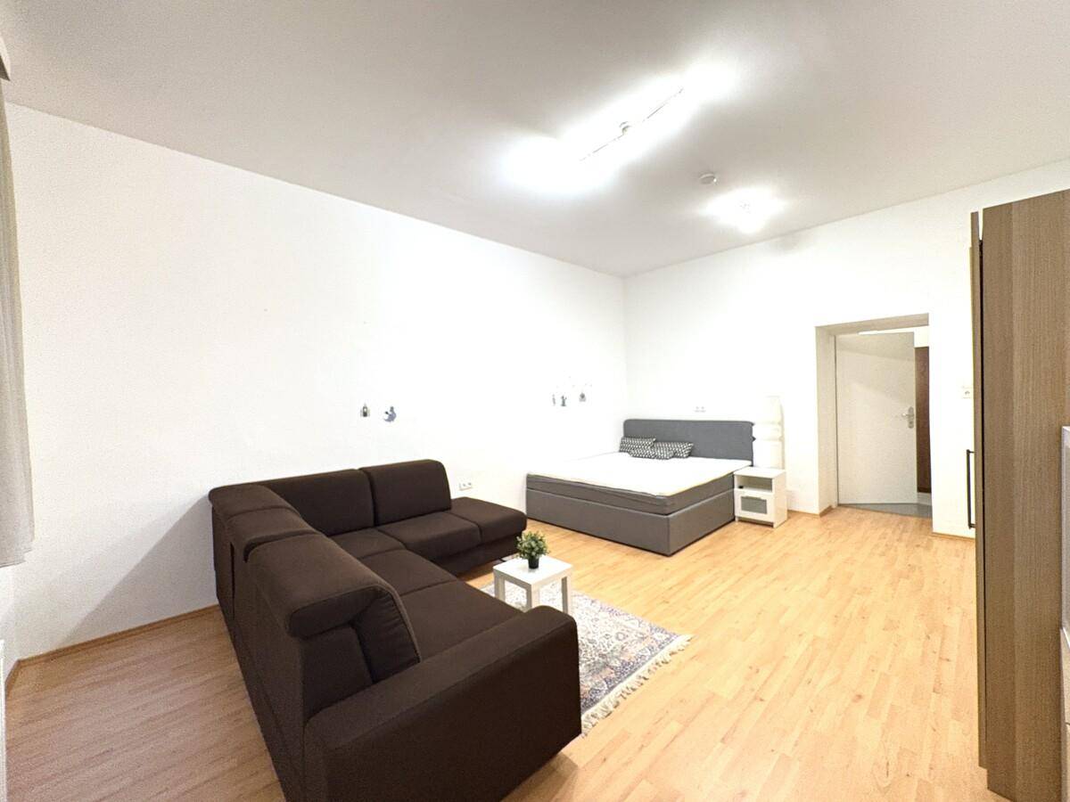 Offener Wohnbereich mit Ecksofa, Bett und Holzboden, ideal für ein Studio-Apartment.