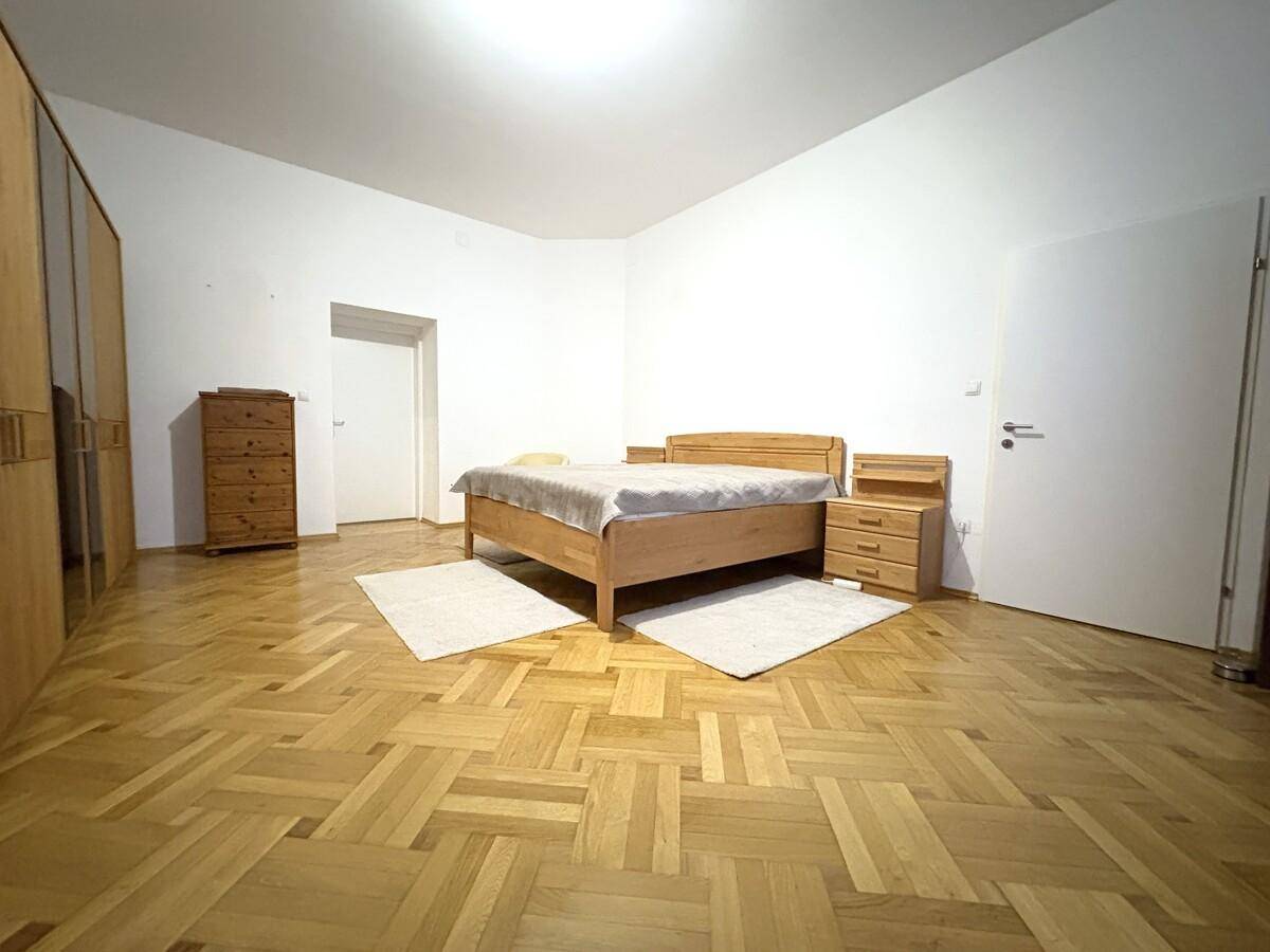 Helles Schlafzimmer mit Holzbett, Nachttischen und Parkettboden in Fischgrätmuster.
