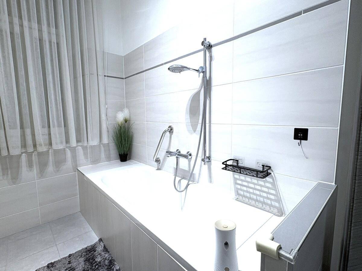 Helle Badewanne mit Duscharmatur und modernen Fliesen in einem gepflegten Badezimmer.