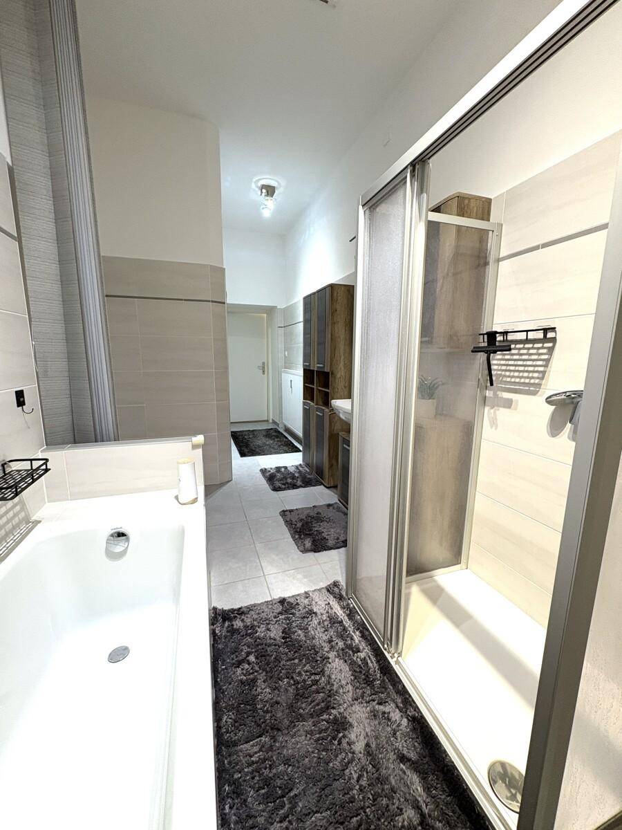 Langes Badezimmer mit Duschkabine, Badewanne und modernen Holzmöbeln.