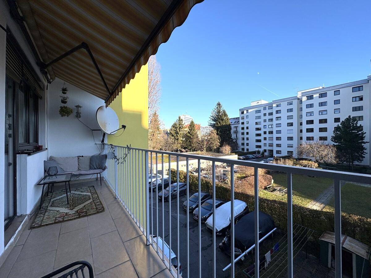 Balkon mit Sitzgelegenheiten und Markise, bietet Blick auf den Parkplatz und die Umgebung.