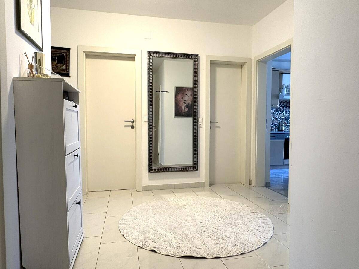 Heller Flur mit Fliesenboden, Schuhschrank und großem Spiegel, der den Raum erweitert.