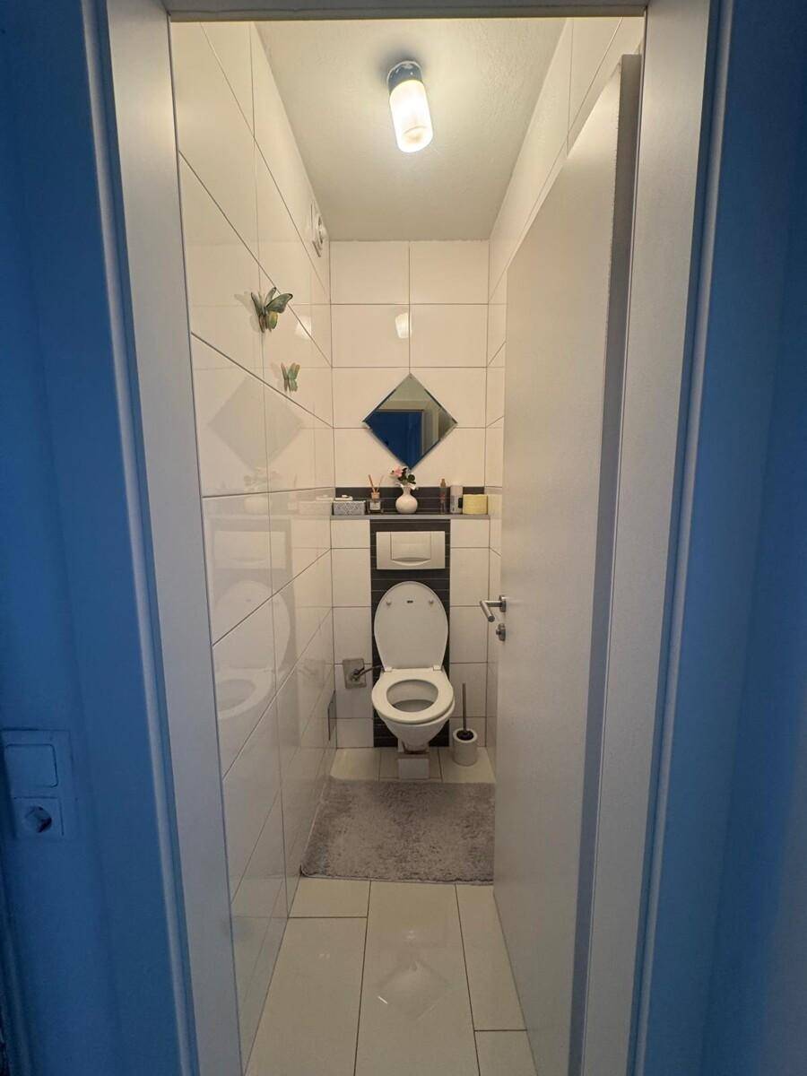 Separates WC mit Toilette und kleinem Spiegel, vollständig gefliest und funktional.