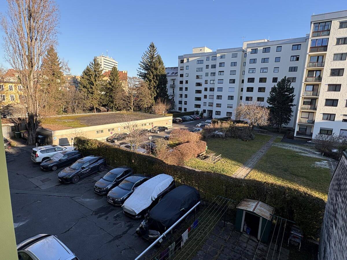 Außenansicht mit Blick auf einen Parkplatz, Grünflächen und umliegende Wohngebäude.