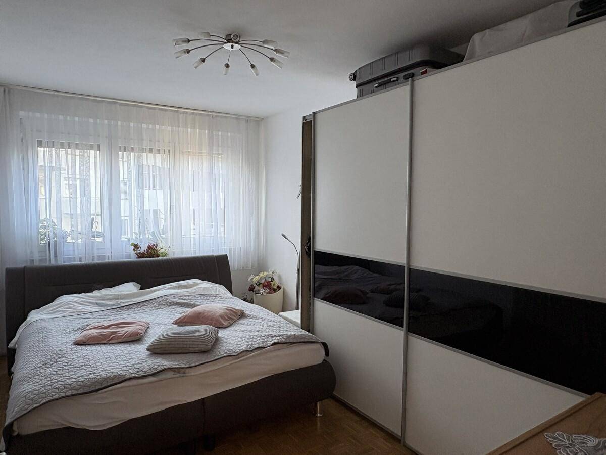 Schlafzimmer mit großem Bett und modernem Schiebetürenschrank, hell durch das Fenster.