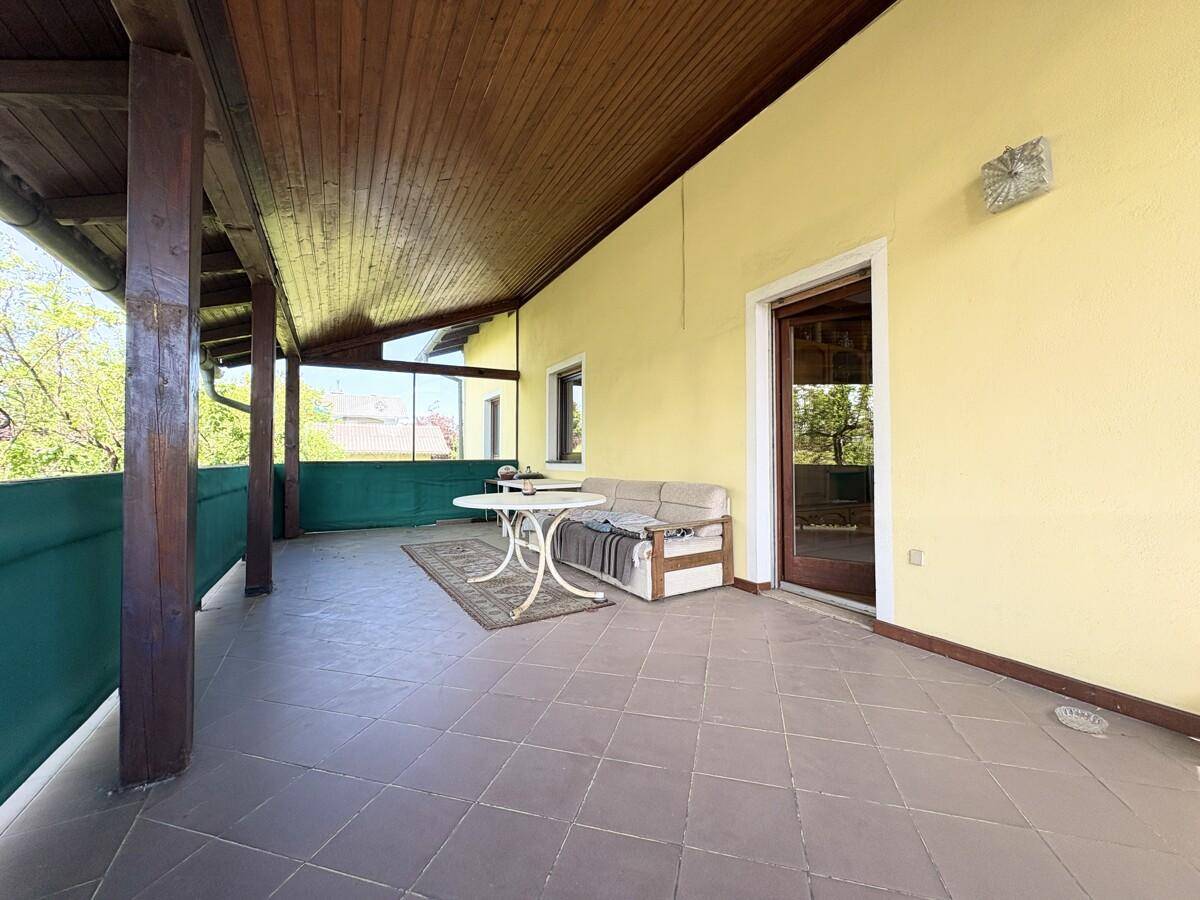 Geräumige überdachte Terrasse mit Fliesenboden und Sitzgelegenheiten, ideal für Entspannung.