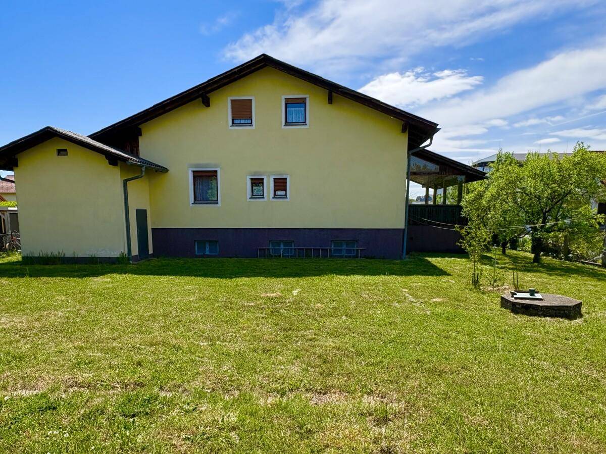 Rückseite des Hauses mit großer Rasenfläche und überdachtem Bereich im Erdgeschoss.