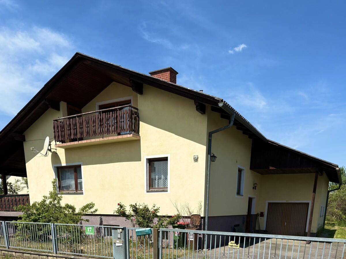 Vorderansicht des gelben Hauses mit Balkon, Satteldach und Einfahrt zur Garage.