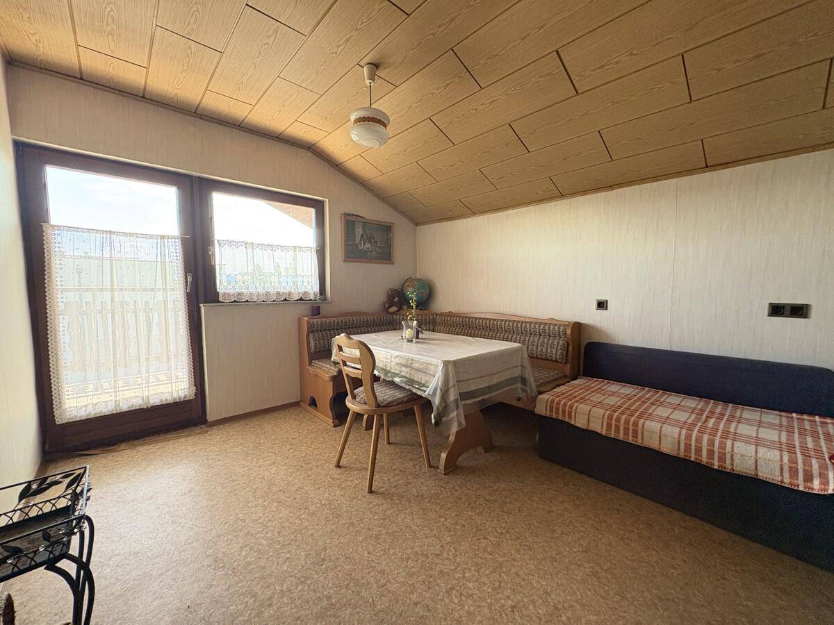 Gemütlicher Wohnbereich im Dachgeschoss mit Holzbalkendecke, Essplatz und Schlafsofa.