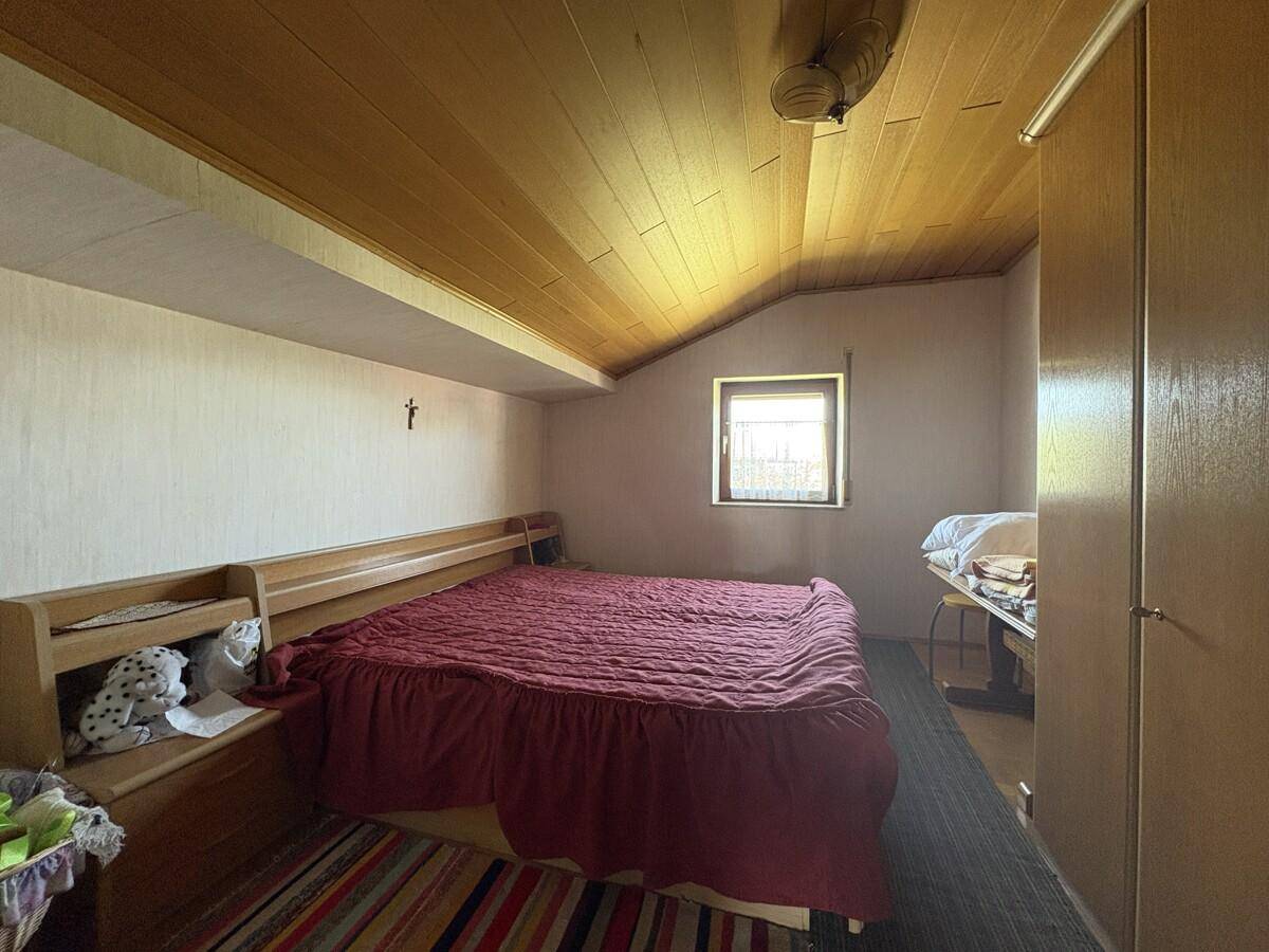 Schlafzimmer im Dachgeschoss mit Holzbett, Holzdecke und schrägen Wänden.
