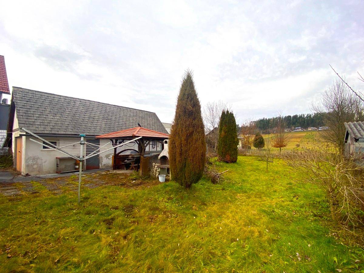 Hinterhof mit Rasenfläche, überdachtem Sitzbereich und weitem Blick in die ländliche Umgebung.