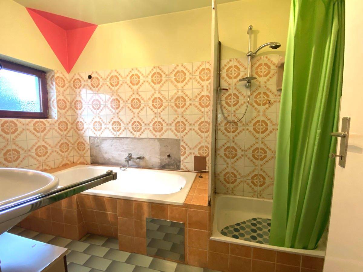 Badezimmer mit gemusterten Fliesen, Badewanne, Dusche und kleinem Fenster.