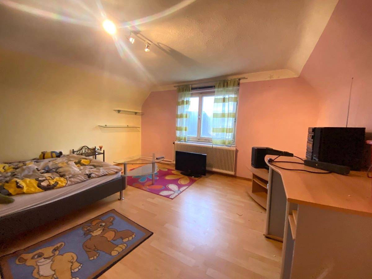 Helles Schlafzimmer im Dachgeschoss mit Schrägen, hellem Holzboden und farbigen Wänden.