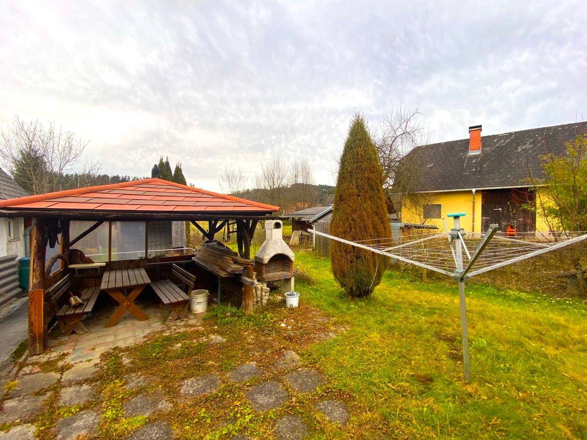 Gemütlicher Gartenbereich mit überdachtem Sitzplatz, Grillstelle und Wäscheständer im Freien.