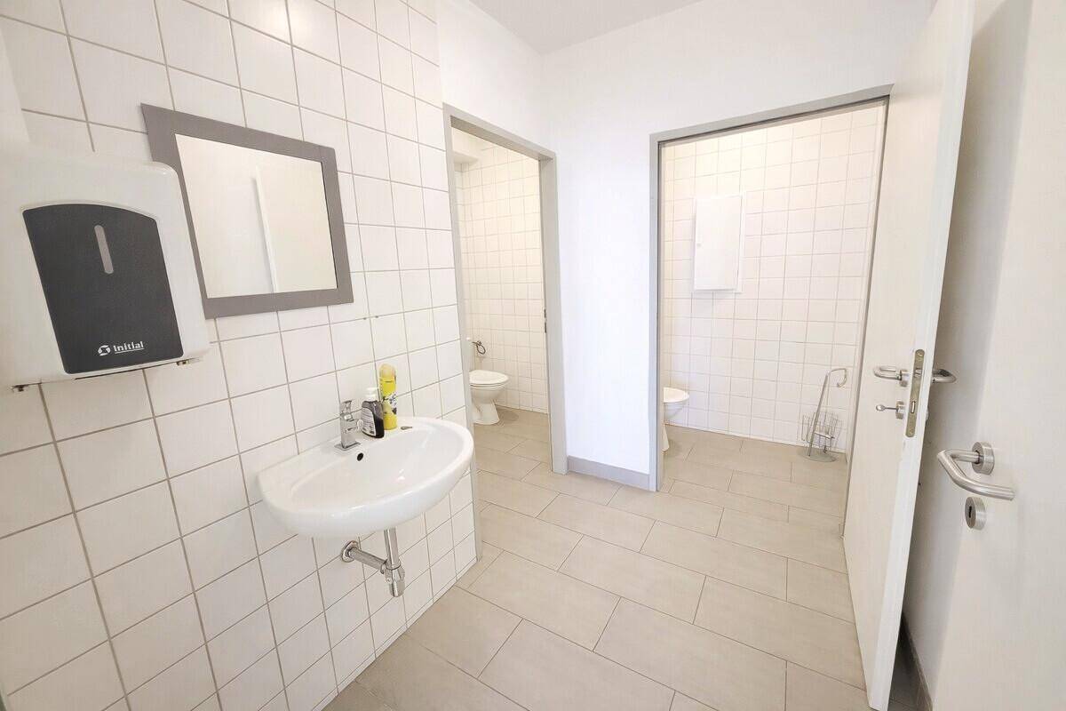 Funktioneller Sanitärbereich mit mehreren Toilettenkabinen und einem Waschbecken mit Spiegel.