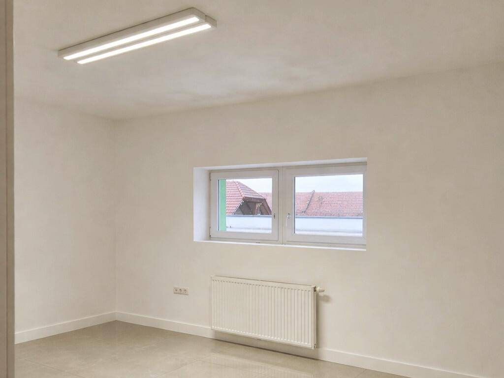 Einfacher, heller Raum mit einem Fenster und einem Heizkörper, ideal für verschiedene Nutzungen.