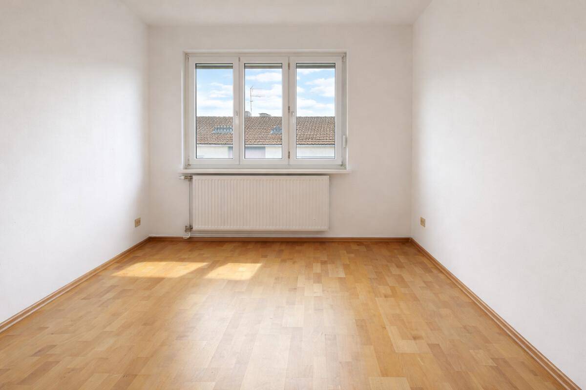 Heller, leerer Raum mit Holzparkettboden und großem Fenster.