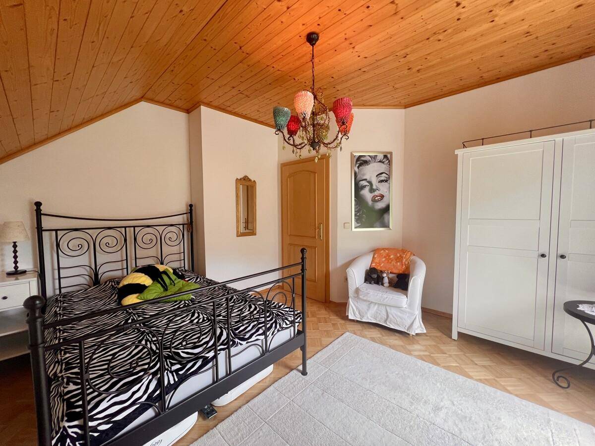 Gemütliches Schlafzimmer mit Holzbalkendecke, schmiedeeisernem Bett und farbenfrohem Kronleuchter.
