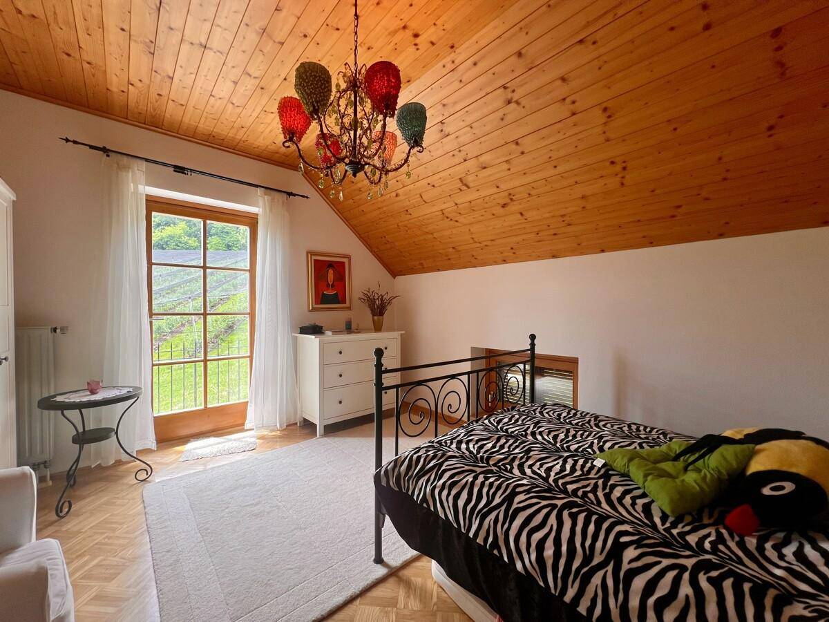 Schlafzimmer im Dachgeschoss mit Holzdecke, Doppelbett und Zugang zum Balkon.