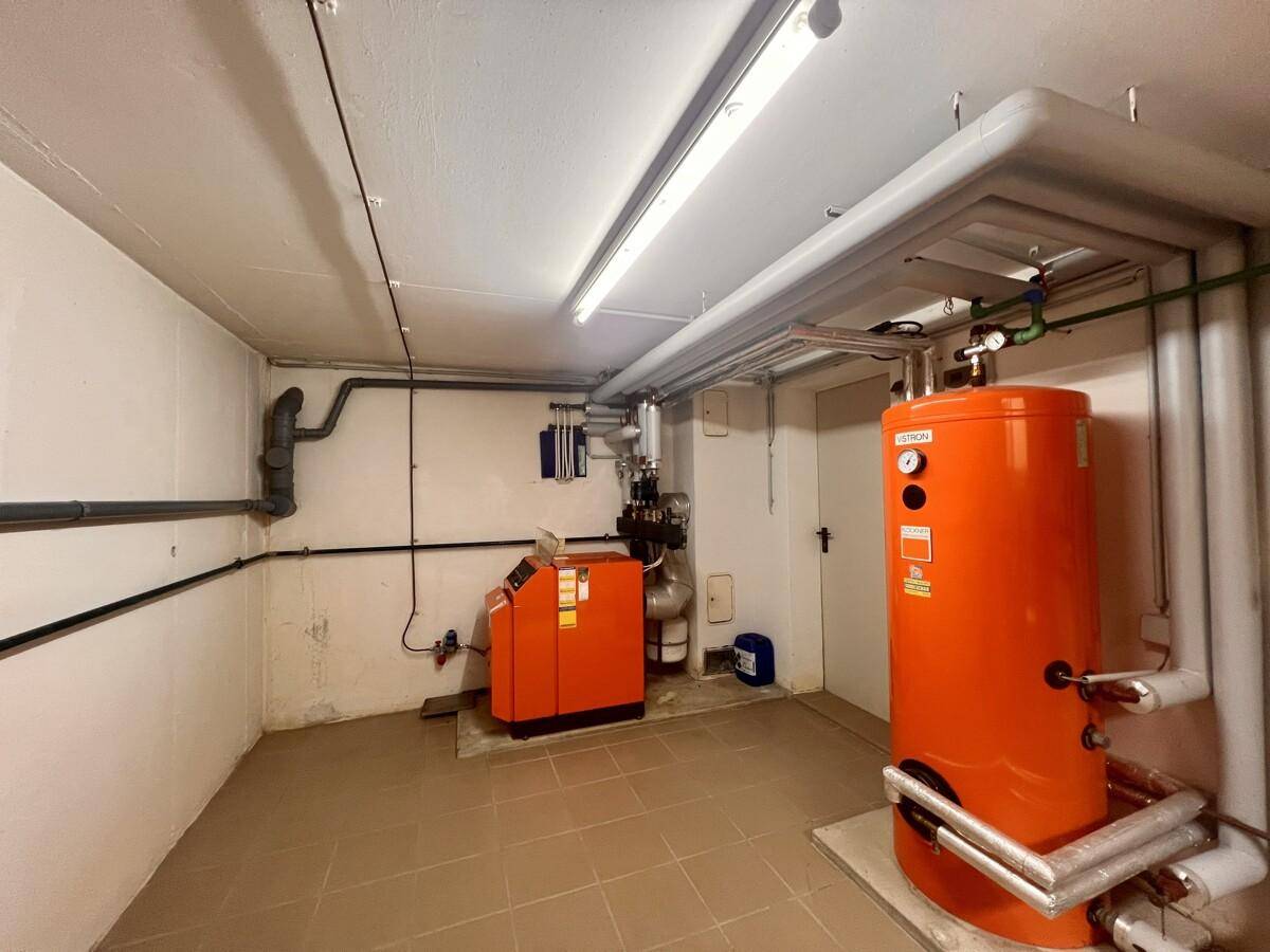 Heizraum mit modernem orangefarbenem Warmwasserspeicher und Heizungsanlage auf gefliestem Boden.