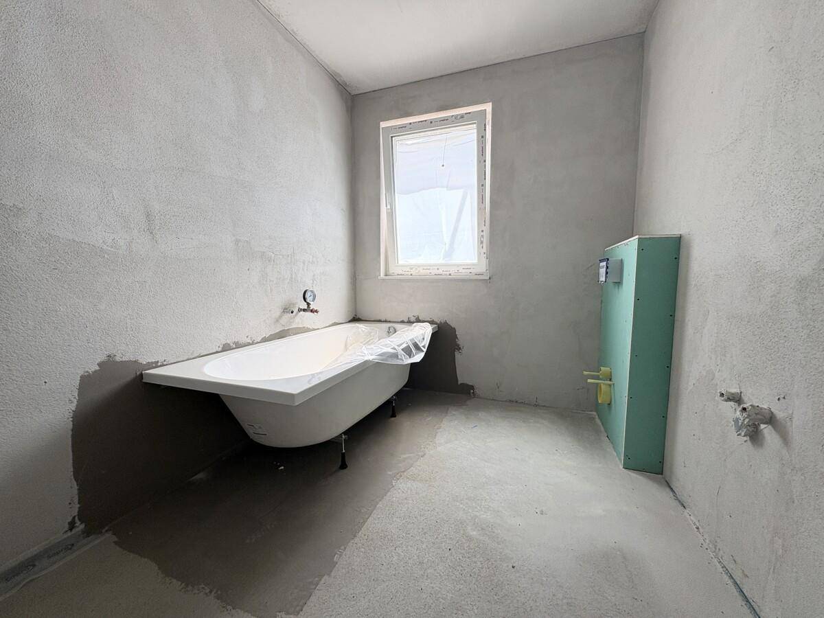 Unfertiges Badezimmer mit einer Badewanne und einem Fenster, bereit für den Ausbau.