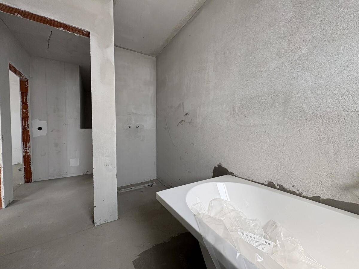 Rohbau eines Badezimmers mit Badewanne und Zugang zu einem weiteren Raum.