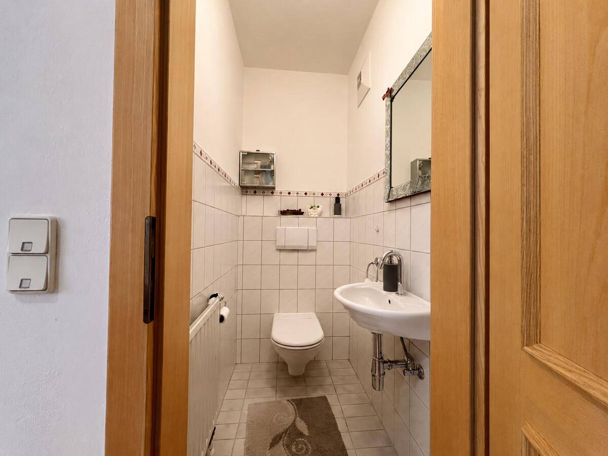 Kleines Gäste-WC mit weißen Fliesen, Wand-WC und Waschbecken.